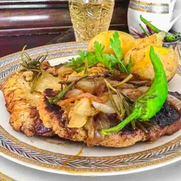 After exhausting days, enjoy a quick fix dinner with a plate of grilled meat topped with onions and garnished with green peppers and herbs. Accompanied by roasted potatoes, the meal is set against a backdrop of champagne and a white teapot on an elegant table setting.