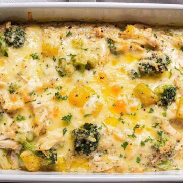 A casserole dish filled with a baked chicken, broccoli, and cheese casserole. The dish features visible pieces of chicken, broccoli florets, and melted cheese, garnished with chopped herbs.