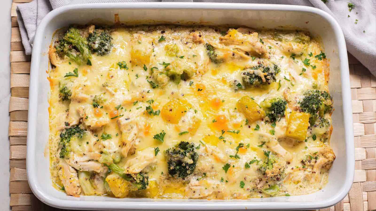 A casserole dish filled with a baked chicken, broccoli, and cheese casserole. The dish features visible pieces of chicken, broccoli florets, and melted cheese, garnished with chopped herbs.