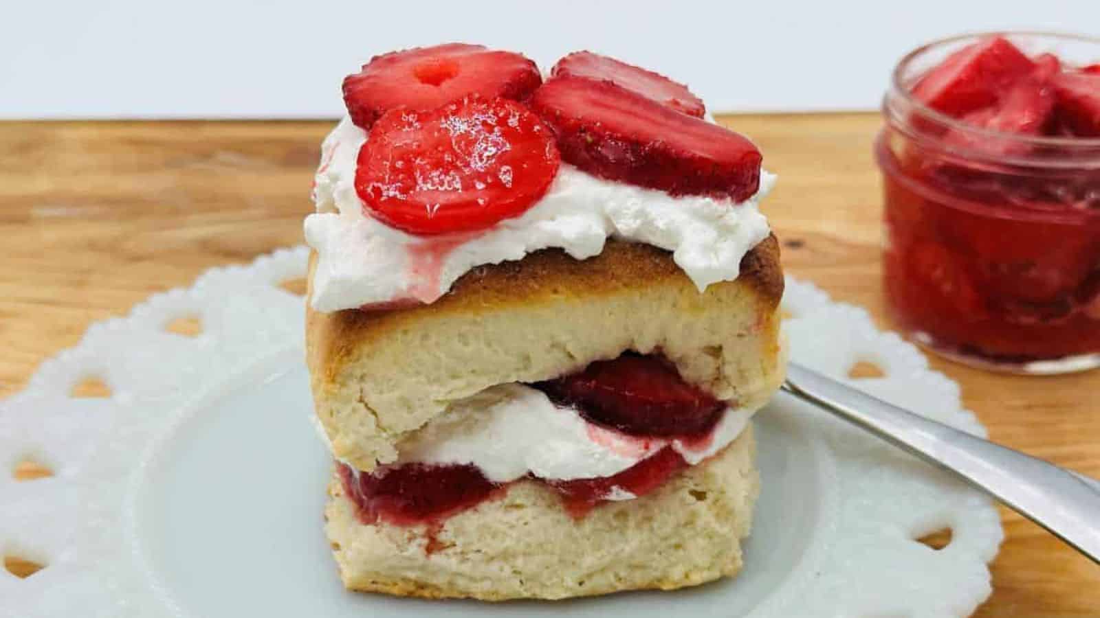 A piece of biscuit with strawberries and whipped cream on a white plate.