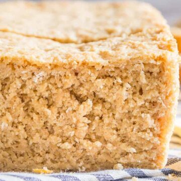 Close-up of a delicious loaf of homemade bread with a rough, textured surface. The bread is placed on a striped cloth, with its soft, beige interior visible due to the way it's sliced. Butter and a knife are visible in the background, reminiscent of inviting bakery scenes.