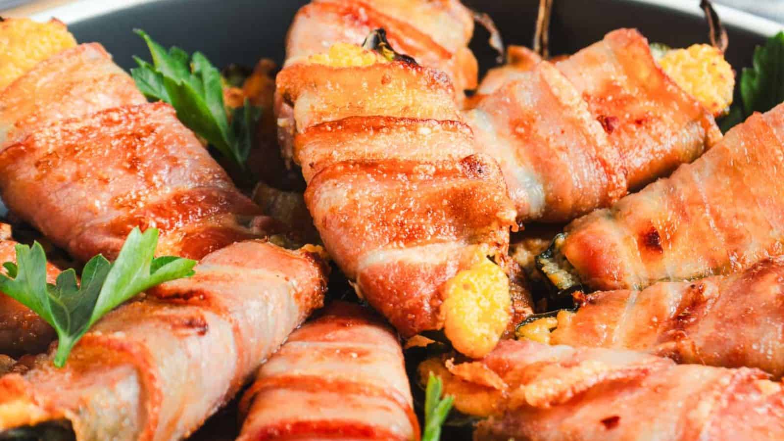 Bacon-wrapped jalapeño poppers are arranged on a plate. The poppers appear golden and crispy, with visible cheese oozing out. Fresh parsley leaves are used as garnish.