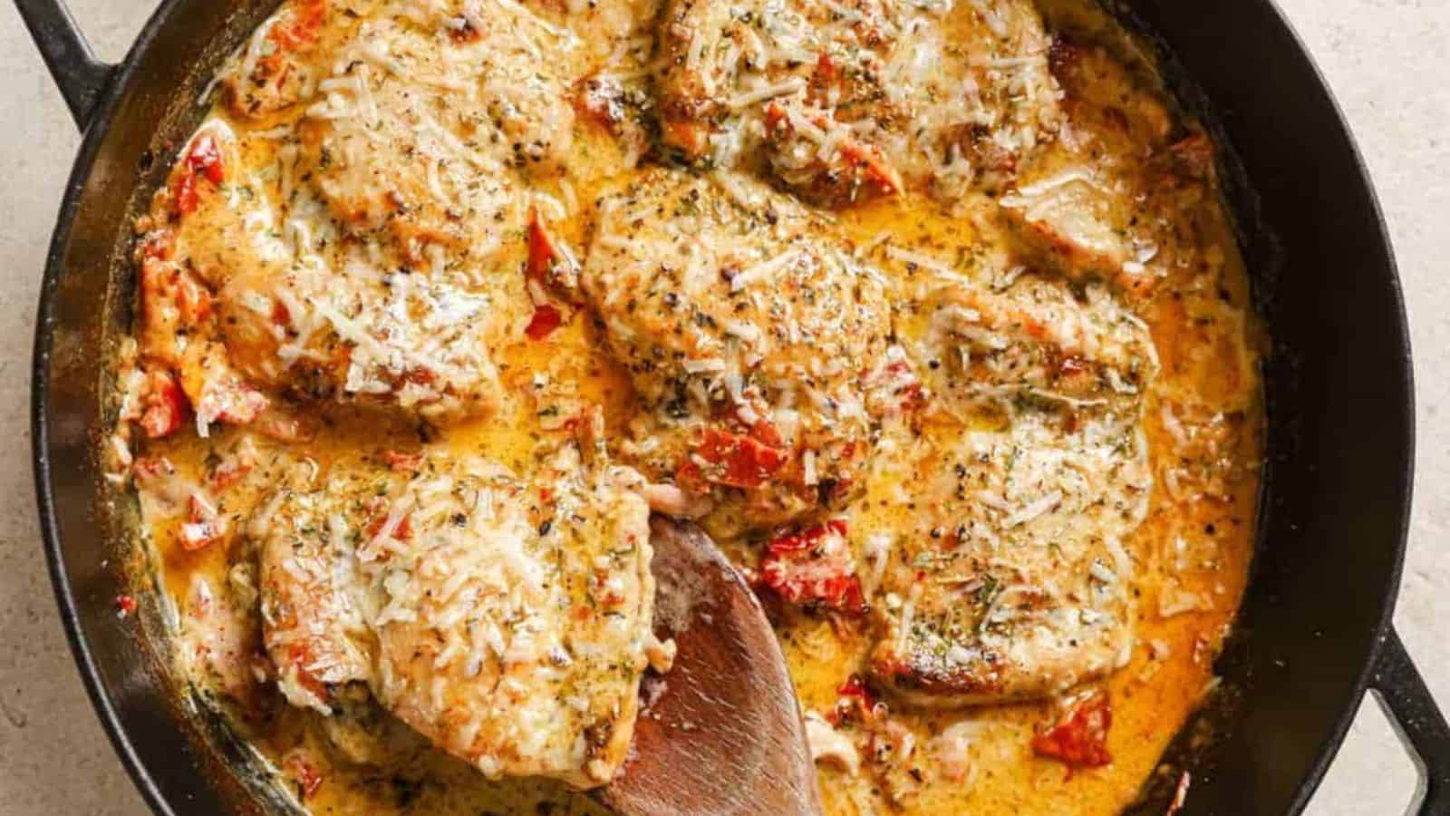 A skillet of creamy sun dried tomato chicken with a wooden spoon.