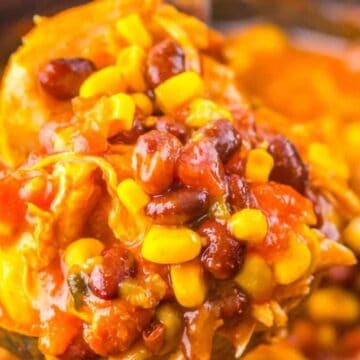 A close-up of a spoonful of chili, showcasing a favorite meal with beans, corn, tomatoes, and shredded chicken in a thick red sauce. The background is blurred, emphasizing the hearty texture and vibrant colors that make it a cherished recipe.