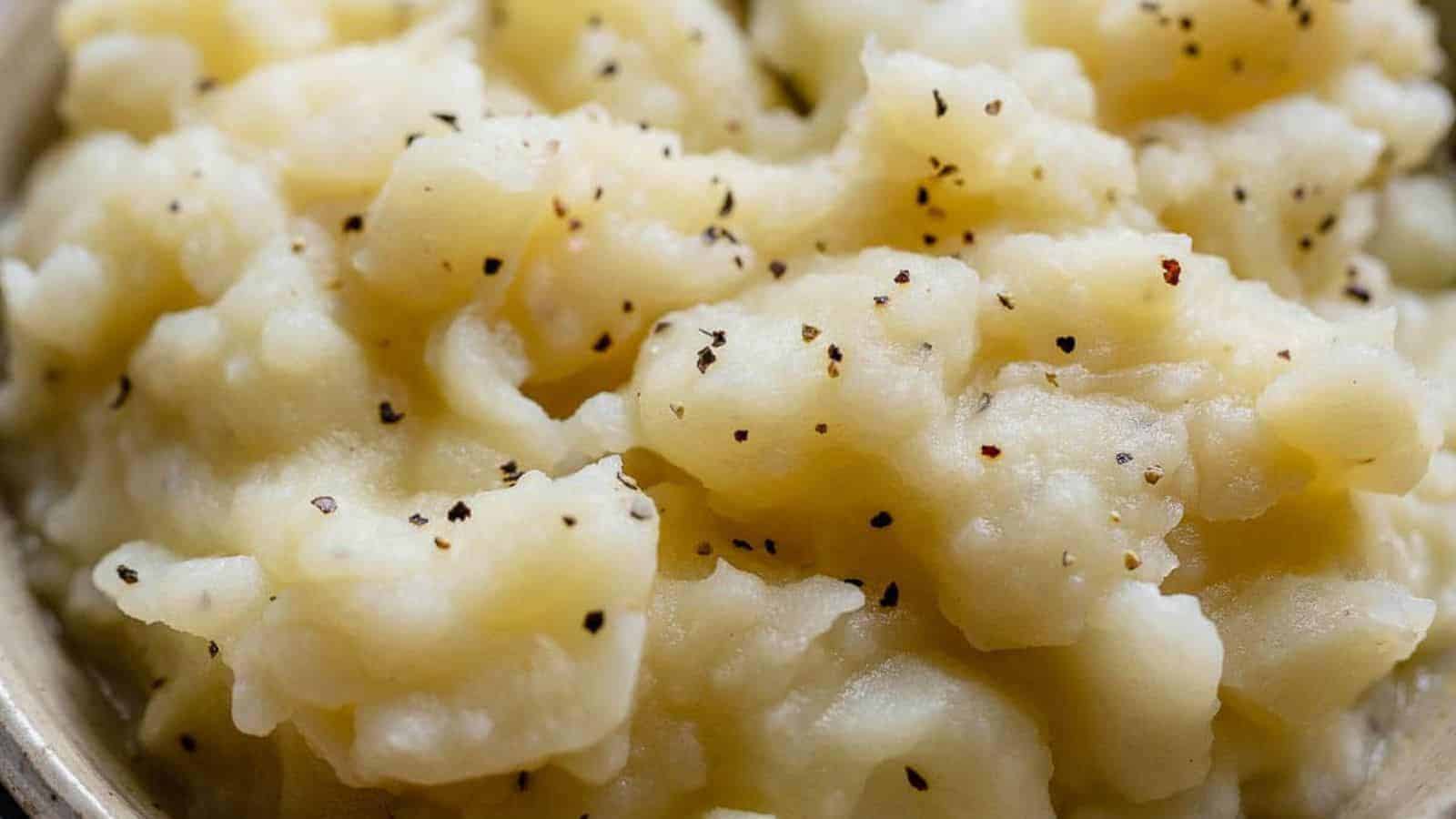 Close-up of creamy mashed potatoes, a classic in Irish recipes, sprinkled with black pepper. The potatoes have a smooth, fluffy texture and occupy most of the frame, highlighting the seasoning and the light cream color of the mash.