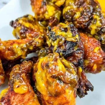 A plate of chicken wings covered in a cooked mango habanero sauce glistens like a BBQ hero. The wings are slightly charred with visible chunks of mango, arranged perfectly on a rectangular white plate, the quintessential centerpiece for any backyard BBQ or grilled meal gathering.
