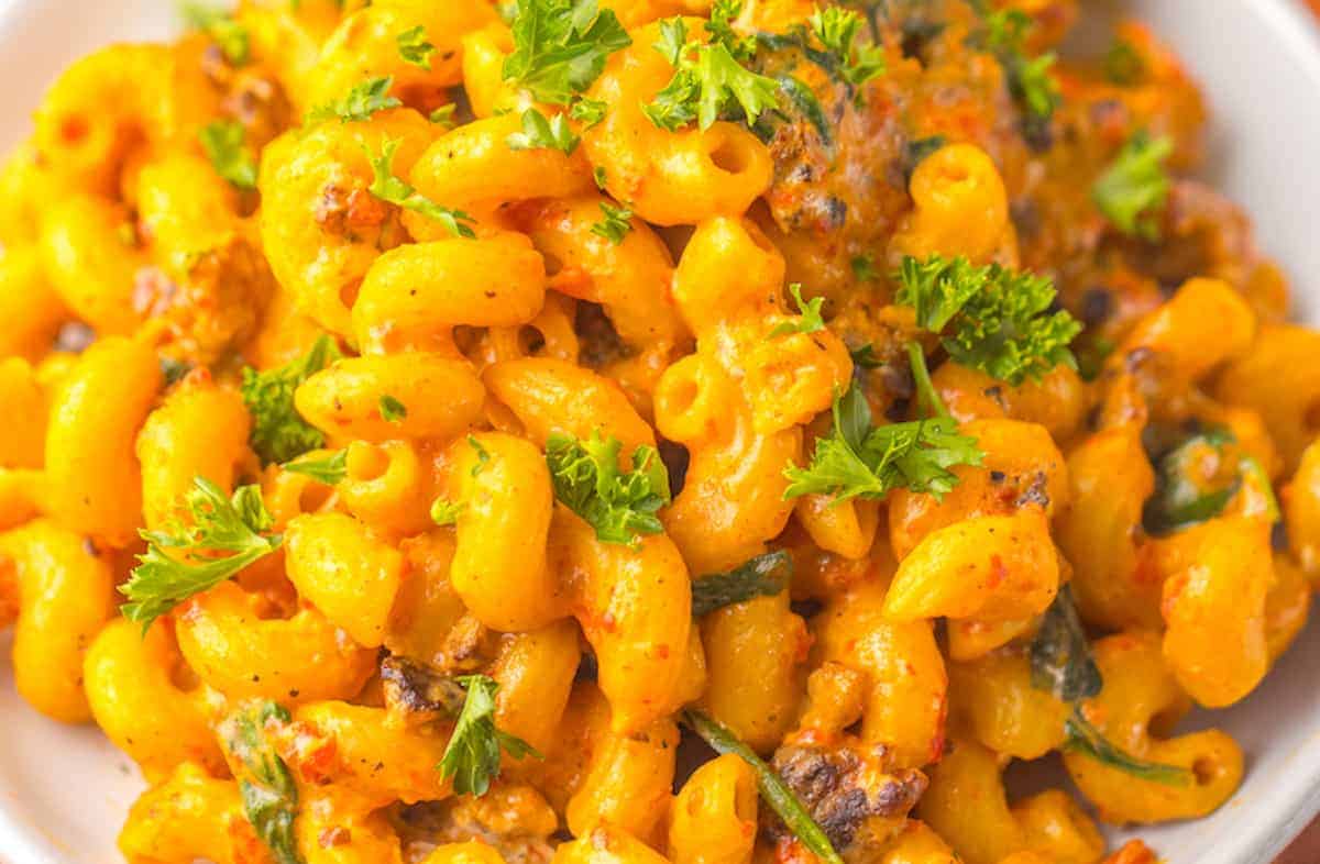 A close-up of a plate of creamy macaroni and cheese, an easy one-pot meal garnished with green parsley. The dish appears rich and cheesy, with visible herbs and spices seamlessly integrated into the pasta.