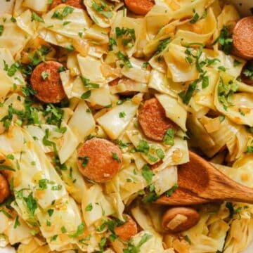 A skillet filled with cooked cabbage, sliced sausage, and chopped parsley—a dish reminiscent of vintage recipes—appears seasoned and is stirred with a wooden spoon. The mix of green, orange, and beige offers not just good food but a visually appealing presentation for every decade.
