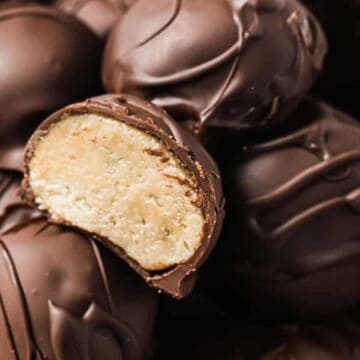 A bowl brimming with several chocolate truffles evokes the comfort of childhood. One truffle is cut in half, unveiling a creamy filling that tempts the senses. With a glossy coating and delicate drizzles, these sugar-filled snacks are a delight to make at home.