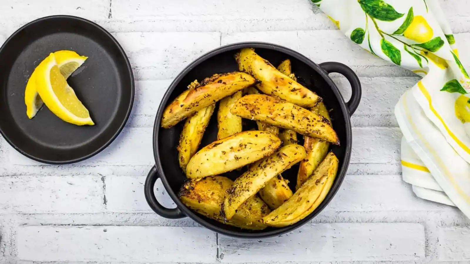 Greek Lemon Garlic Potatoes in a black dish with lemon in the background.