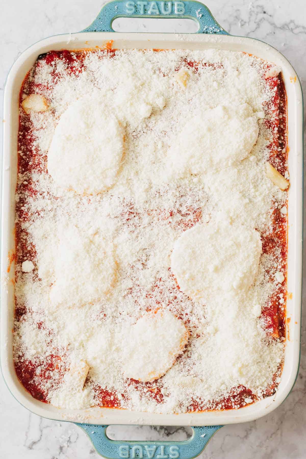 A rectangular baking dish filled with chicken parmesan, topped with tangy tomato sauce and a layer of cottage cheese melted over tender chicken pieces. The blue handles of the dish peek through invitingly.