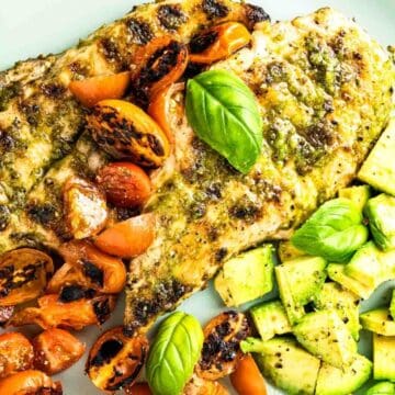 Grilled chicken breasts on a plate with charred cherry tomatoes, diced avocado, and basil leaves make a perfect choice for quick lunches. The chicken is seasoned with herbs, and the plate is artfully arranged for a colorful presentation.