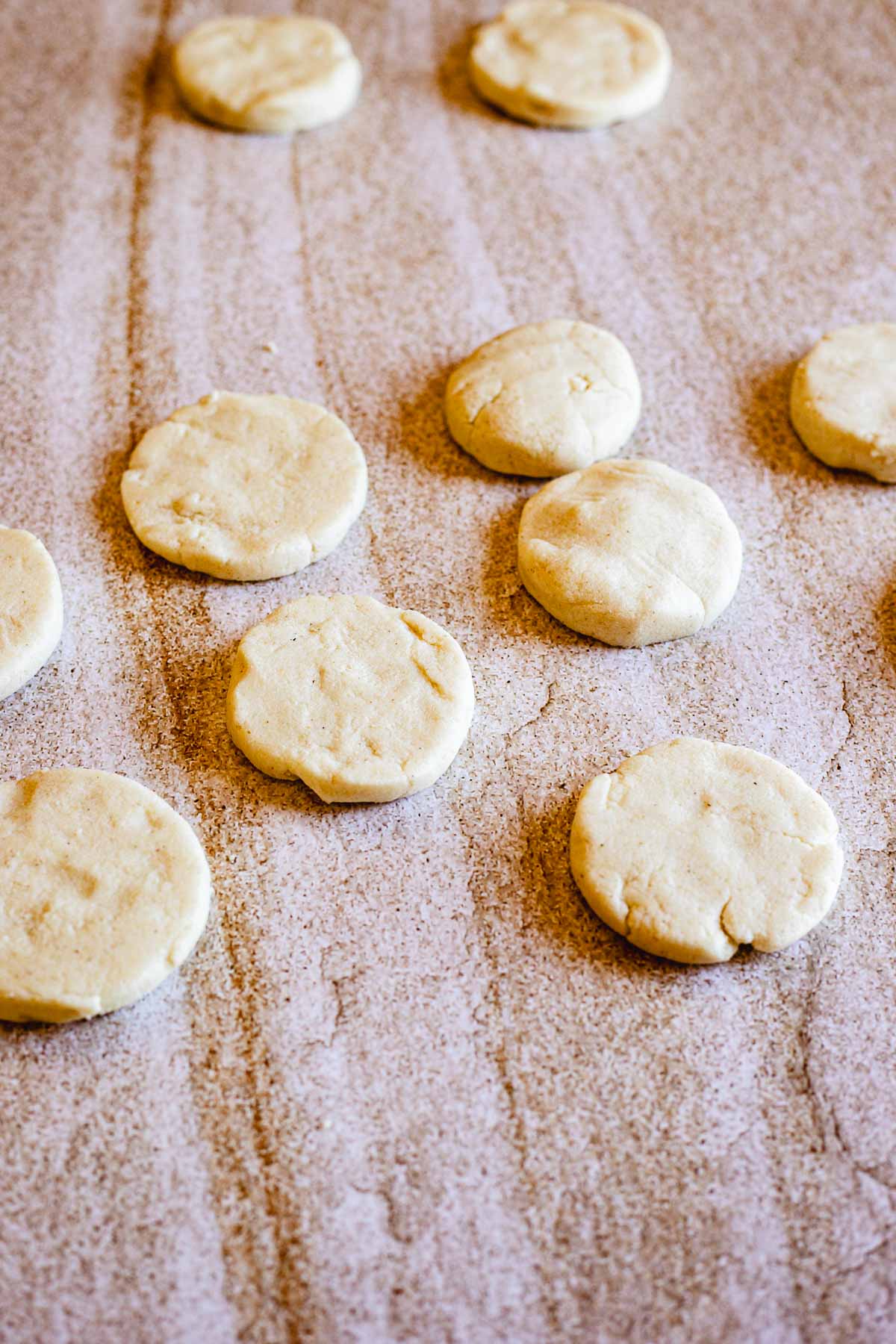 Several round, unbaked dough discs are evenly spaced on a lightly floured wooden surface, ready to become delicious Colombian arepas using a traditional arepa recipe.