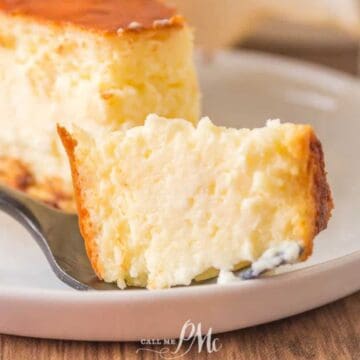 A close-up of a slice of cheesecake on a white plate, with a fork holding a bite-sized piece in the foreground. The creamy texture and golden-brown top make it one of those desserts that always means no leftovers.
