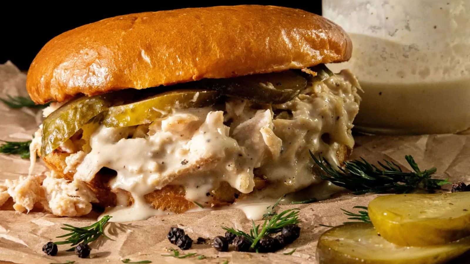 Two Alabama Chopped Chicken Sandwiches with pulled chicken, creamy Alabama white BBQ sauce, and pickle slices on shiny, toasted buns, served on a decorative plate.