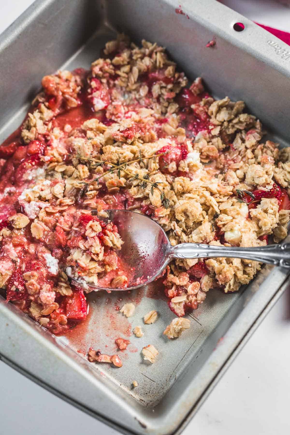 Balsamic Strawberry Crisp With Goat Cheese : At the Immigrant's Table 9 A square metal baking pan containing a partially served Balsamic Strawberry Crisp with a crumbly oat topping and red fruit filling. A metal spoon rests in the dish, with some filling and crumbs on it.