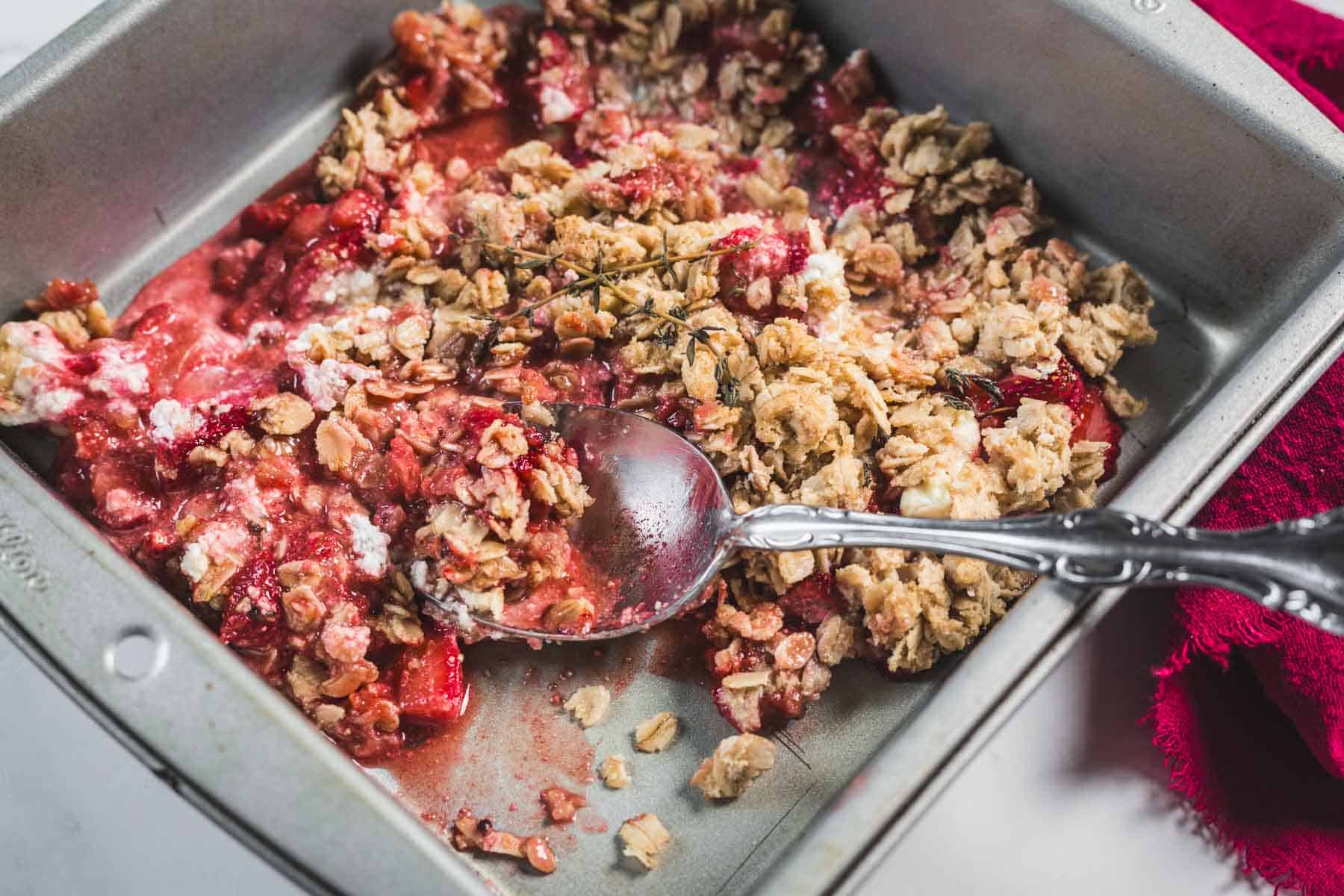 Balsamic Strawberry Crisp With Goat Cheese : At the Immigrant's Table 7 A metal baking pan containing a partially served Balsamic Strawberry Crisp with an oat topping and a silver spoon. Some of the baked fruit and oat crumble mixture has been scooped out, revealing the red strawberry balsamic dessert filling.