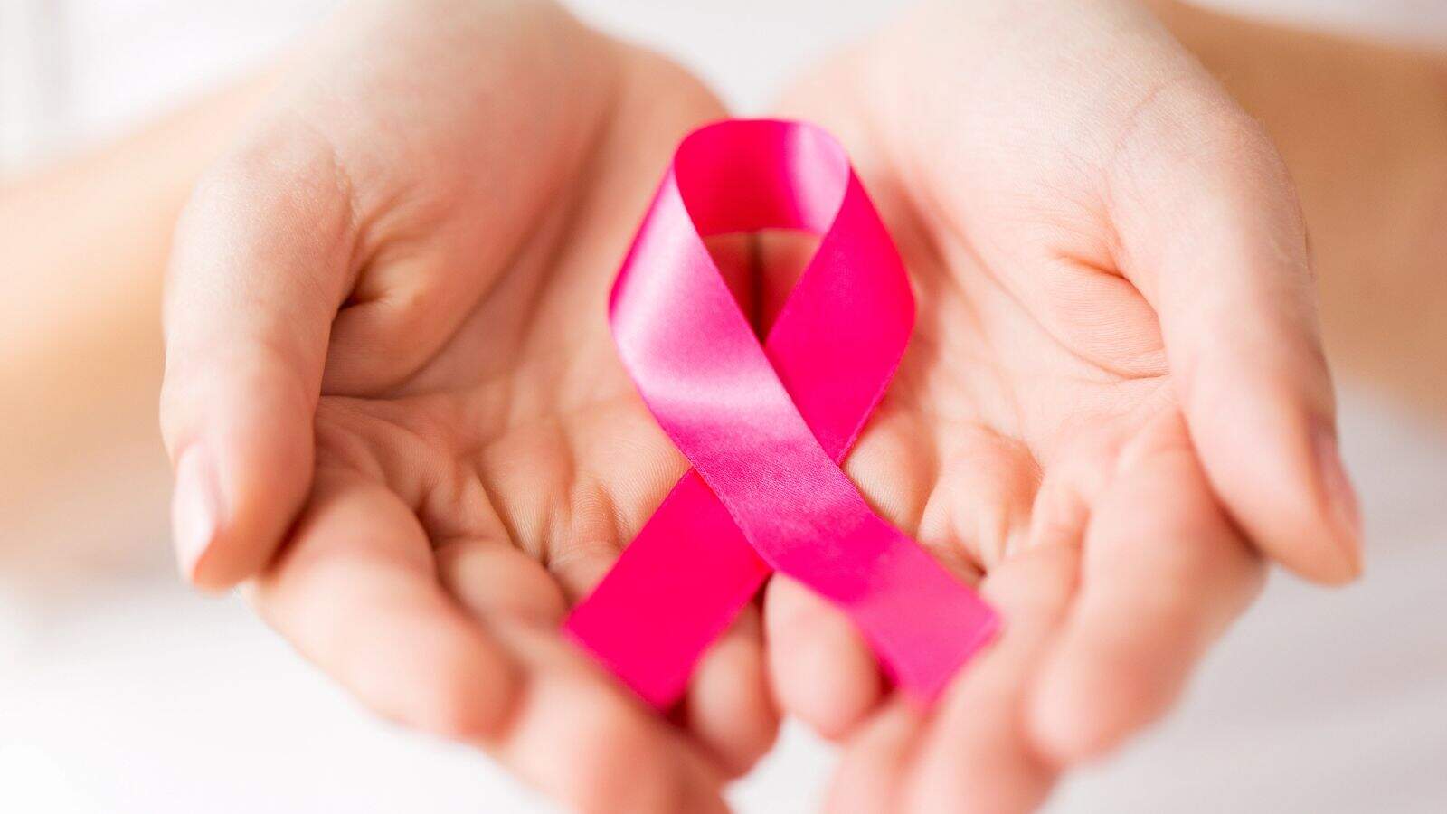 A pair of cupped hands holding a pink ribbon, which is a widely recognized symbol for breast cancer awareness.