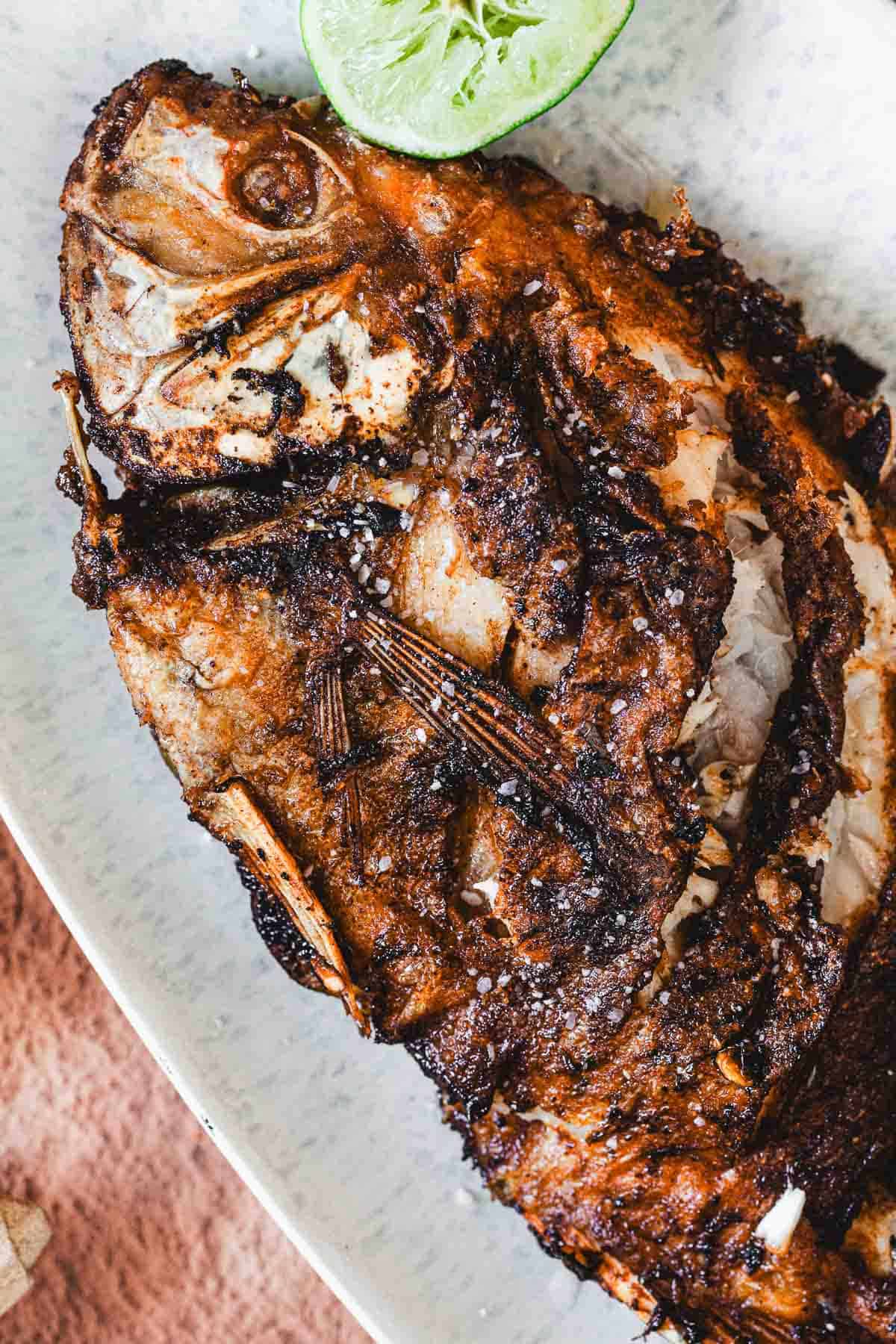 A close-up of a whole fried mojarra with crispy, browned skin, served on a white plate with a wedge of lime near the fish’s head—a classic dish in Colombian cuisine.