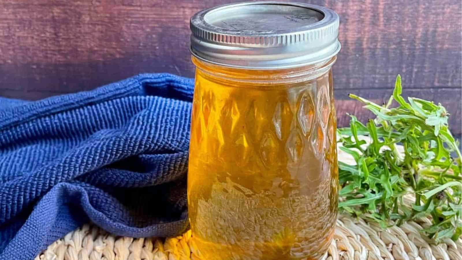 Dandelion jelly in a mason jar with dandelions and a blue cloth.