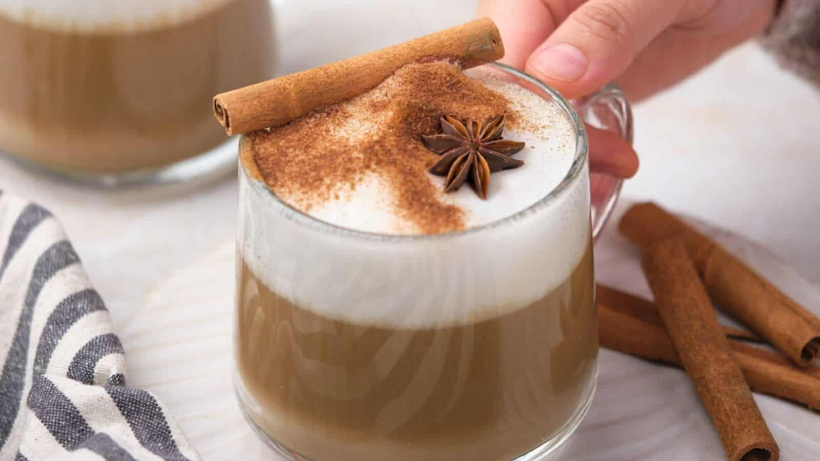 Two glass mugs of dirty chai tea latte, with one being held by a hand.