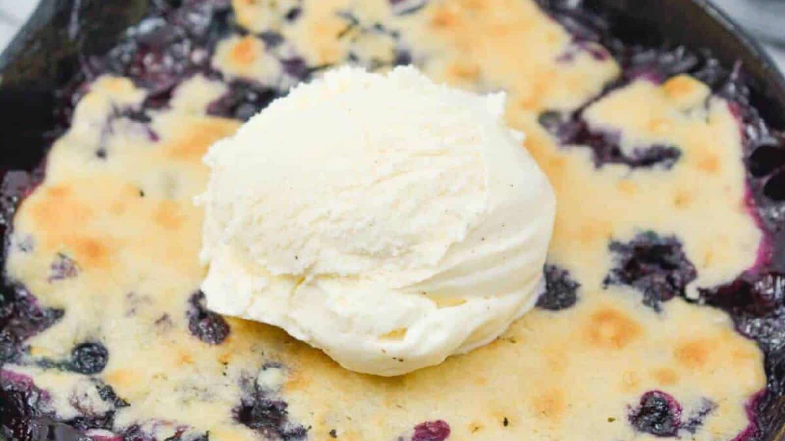 Mini blueberry cobbler in small cast iron skillet with scoop of vanilla ice cream.