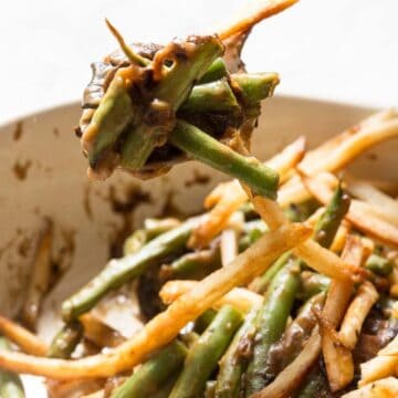 A dish with french fries and green beans in a creamy brown sauce, with a spoon lifting a portion from a white pan.