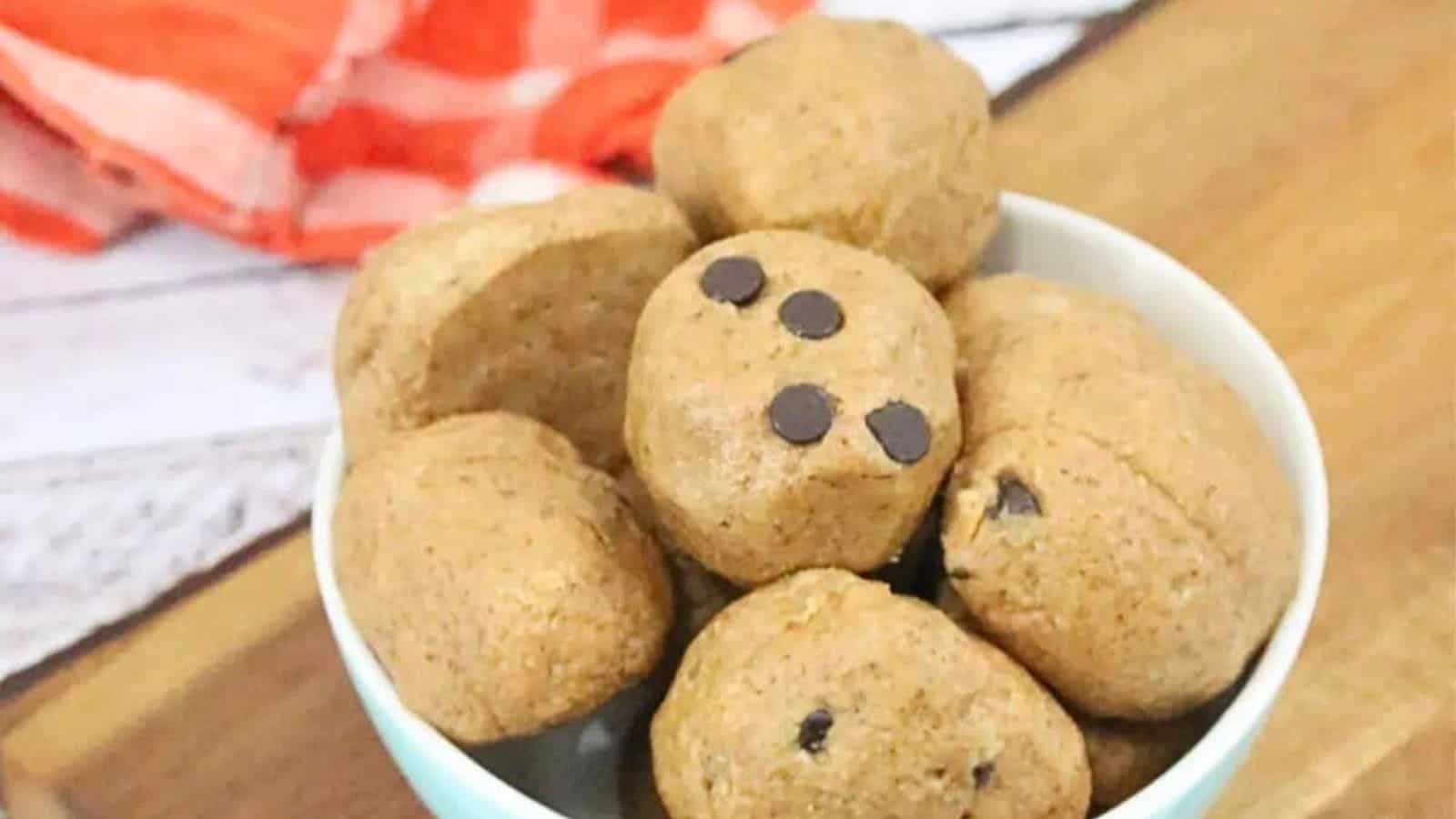 Paleo cookie dough ball being held between fingers with more in a bowl.