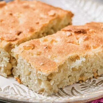 Two rectangular pieces of homemade cake or bread with a golden-brown crust and a moist, dense interior are placed on a decorative ceramic plate.