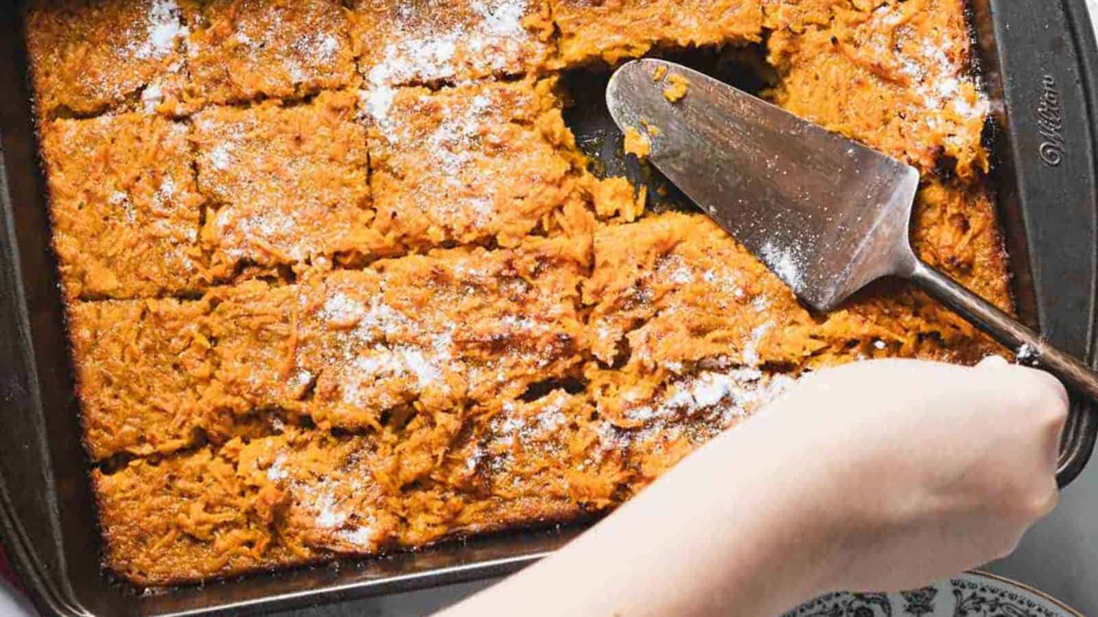 A delightful slice of carrot cake with a dollop of whipped cream graces a decorative black and white plate. A fork rests invitingly on the cake while a white and blue cup peeks from the background, almost like the perfect ending to a recipe for an unforgettable carrot casserole.