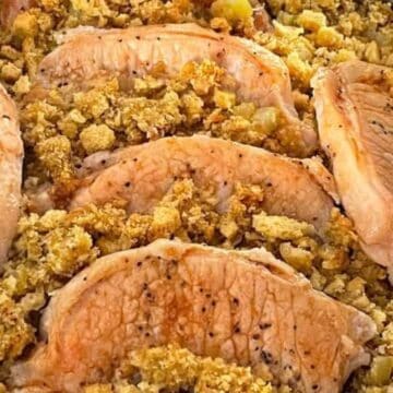 Five seasoned pork chops are arranged on top of a bed of cooked stuffing with visible bread cubes and celery in a baking dish. The stuffing appears golden and textured.