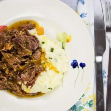 A plate of pot roast with bacon and mashed potatoes with gravy.
