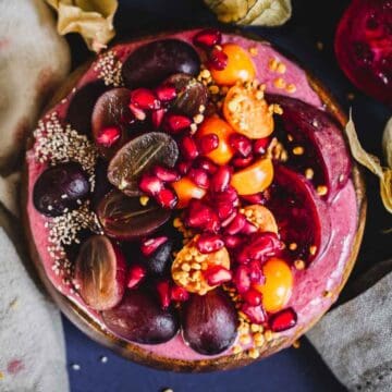 A Prickly Pear Smoothie Bowl topped with halved red grapes, golden berries, pomegranate seeds, bee pollen, and chia seeds, all arranged neatly on a vibrant pink smoothie base.