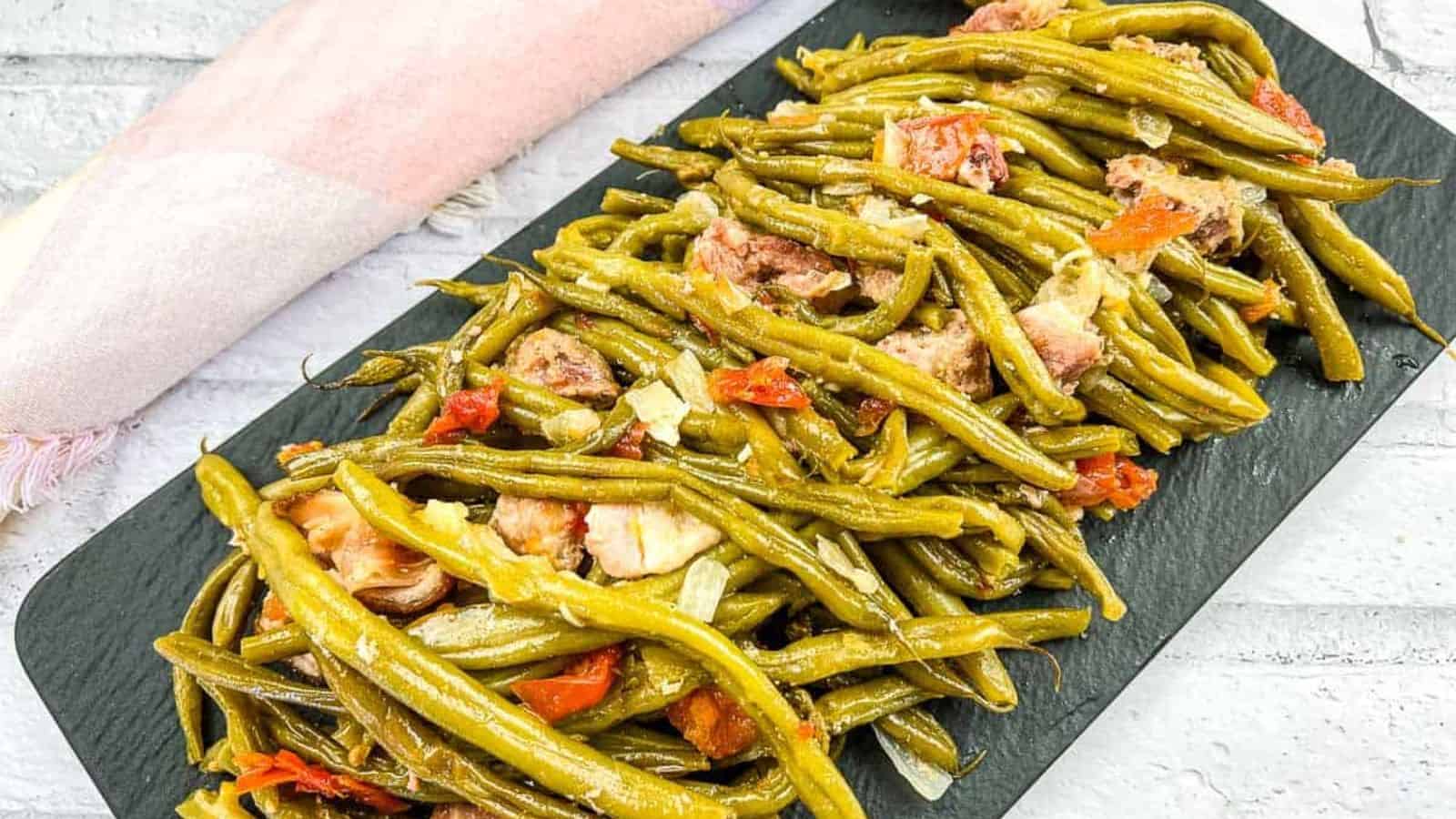 Green beans with pork on a black plate.