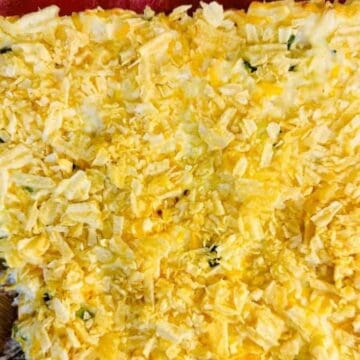 A casserole dish filled with a baked, golden-brown topping of crushed chips, with a wooden spoon resting in one corner where a portion has been served.
