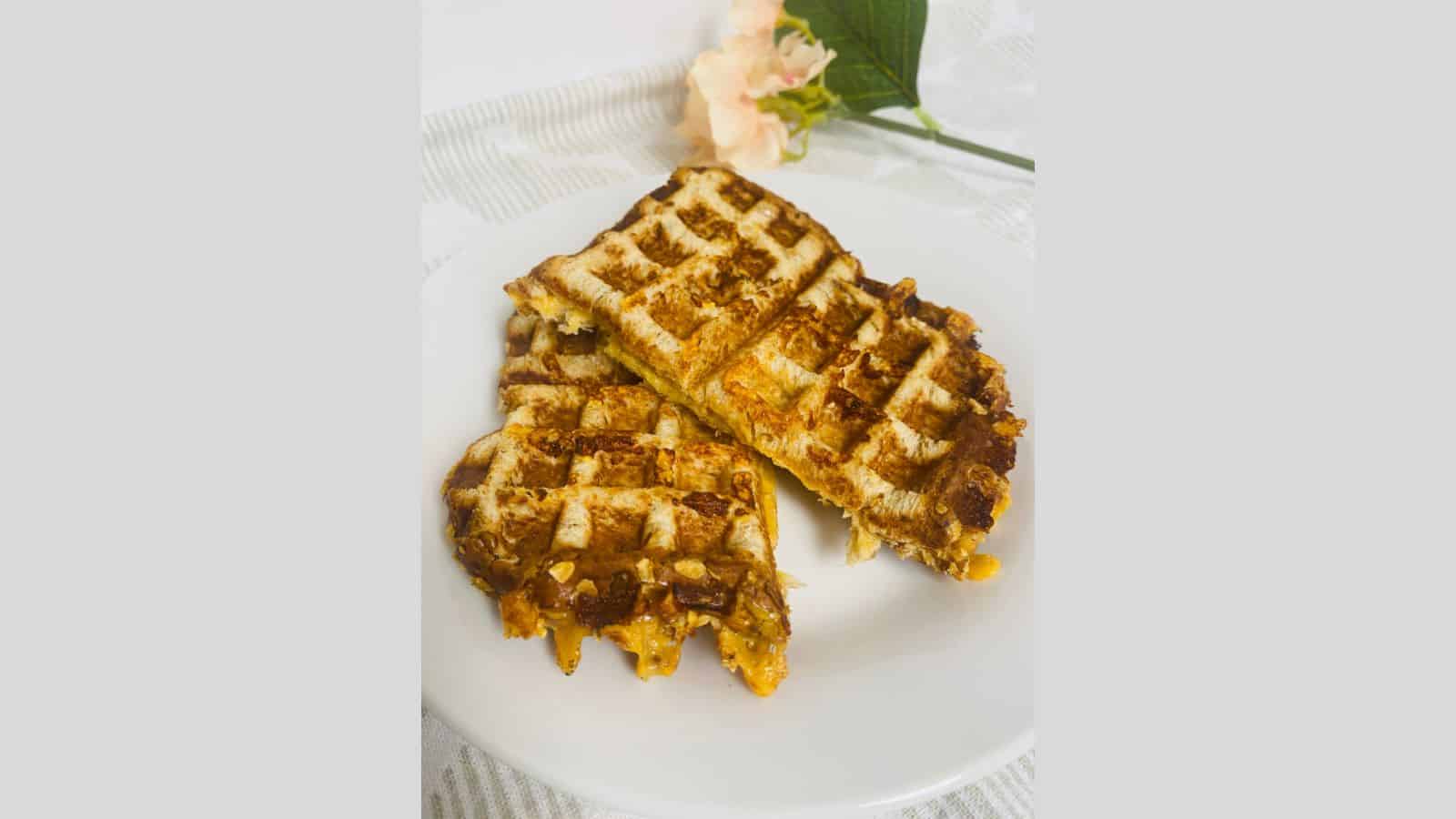 Two grilled sandwiches with visible grill marks are cut in half and stacked on a white plate—a tasty nod to classic recipes. A pale pink flower and green leaves decorate the background on a white surface.