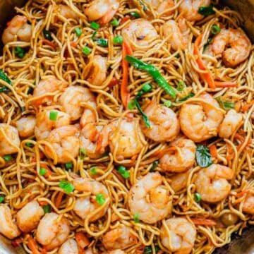 A large skillet filled with shrimp, stir-fried noodles, green onions, and vegetables, with a small bowl of chopped green onions on the side.