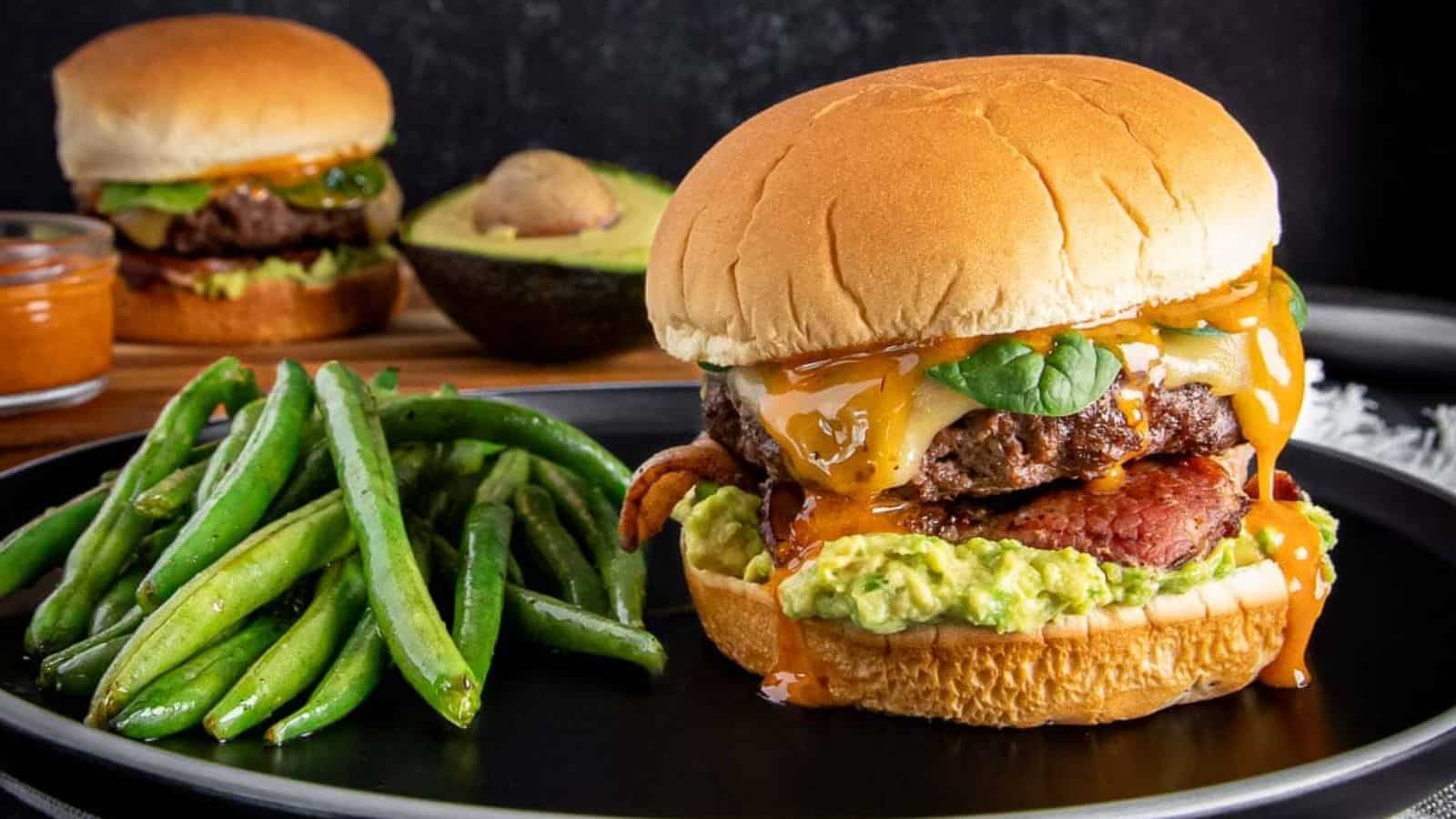 An up-close shot of bacon-avocado ground beef burger on a flat white surface.