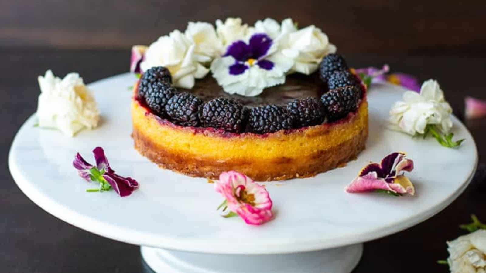 Overhead shot of a blackberry lime tart on a white plate surrounded by edible flowers.