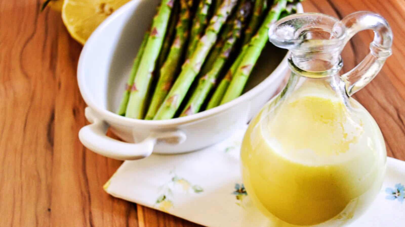 A jar of hollandaise sauce next to a bowl of asparagus.
