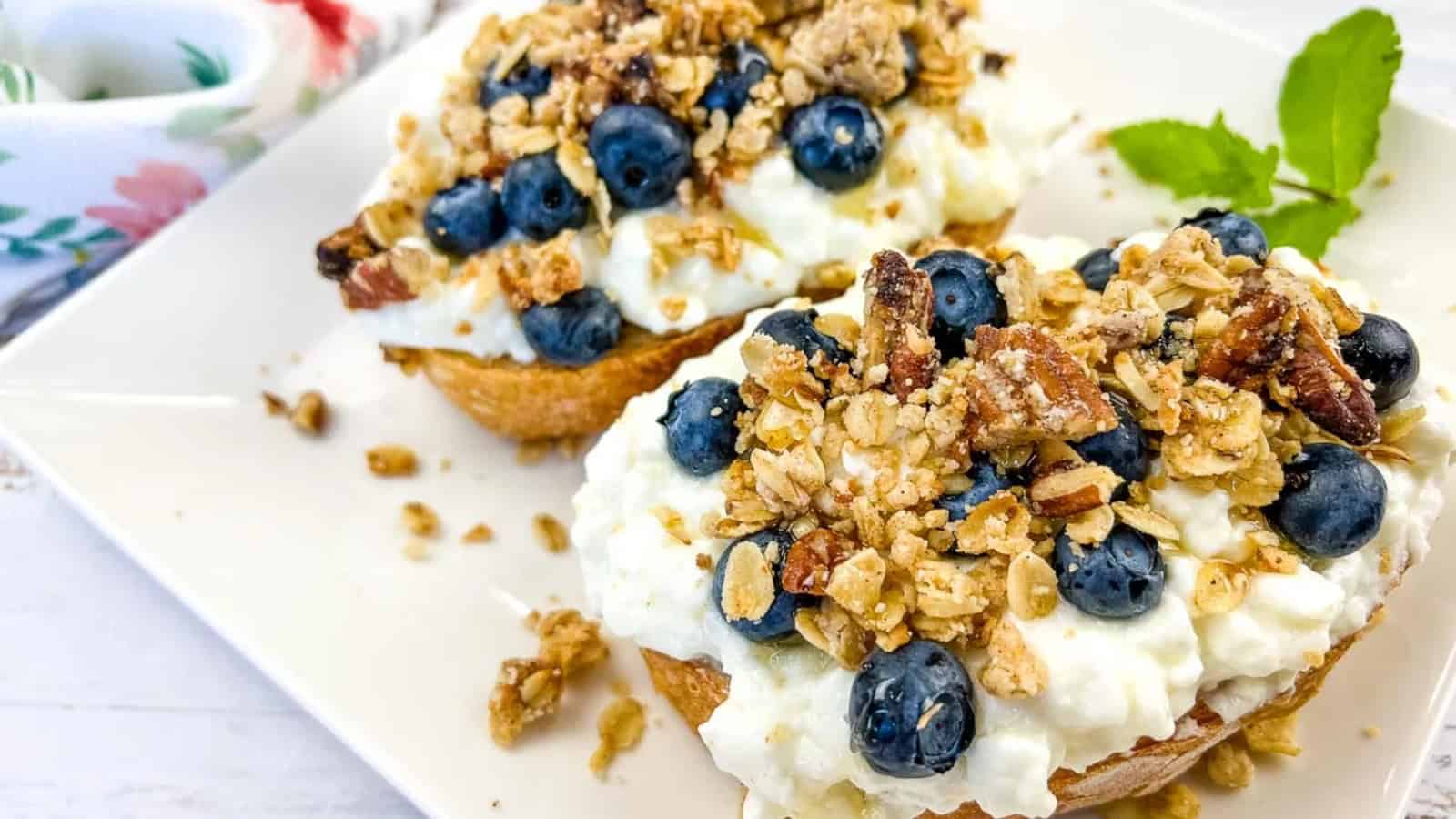 A plate of cottage cheese toast with blueberries, next to a honey dipper.