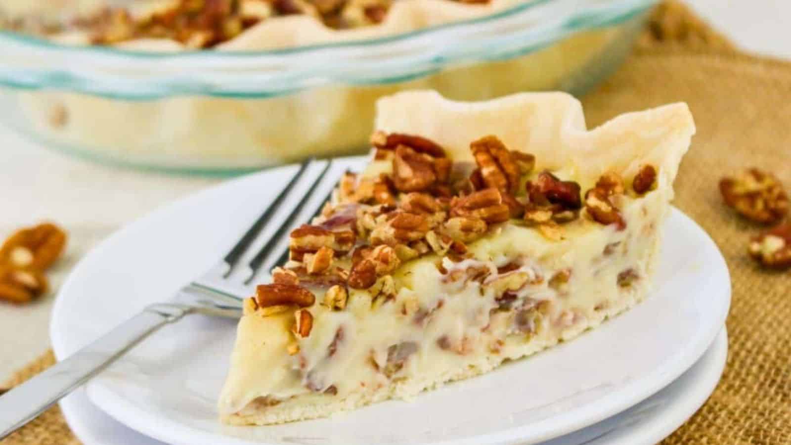 Slice of pecan pie on a white plate with a fork, placed on a burlap surface. The pie has a pastry crust, creamy filling, and is topped with chopped pecans.
