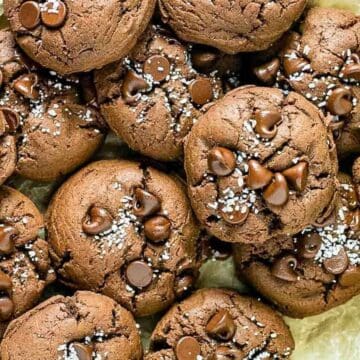 A batch of chocolate treats is piled on parchment paper, perfect for turning around a bad day. The cookies are studded with chocolate chips and sprinkled with coarse salt on top.