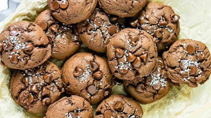 A batch of chocolate treats is piled on parchment paper, perfect for turning around a bad day. The cookies are studded with chocolate chips and sprinkled with coarse salt on top.
