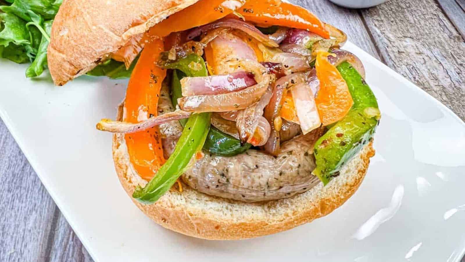 A sandwich with grilled sausage & peppers, and onions on a plate.