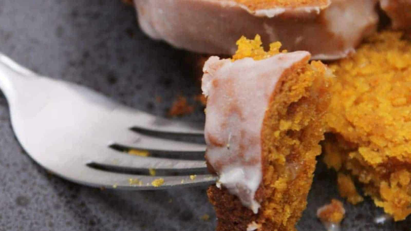 A fork holds a piece of pumpkin loaf with icing on a gray plate.
