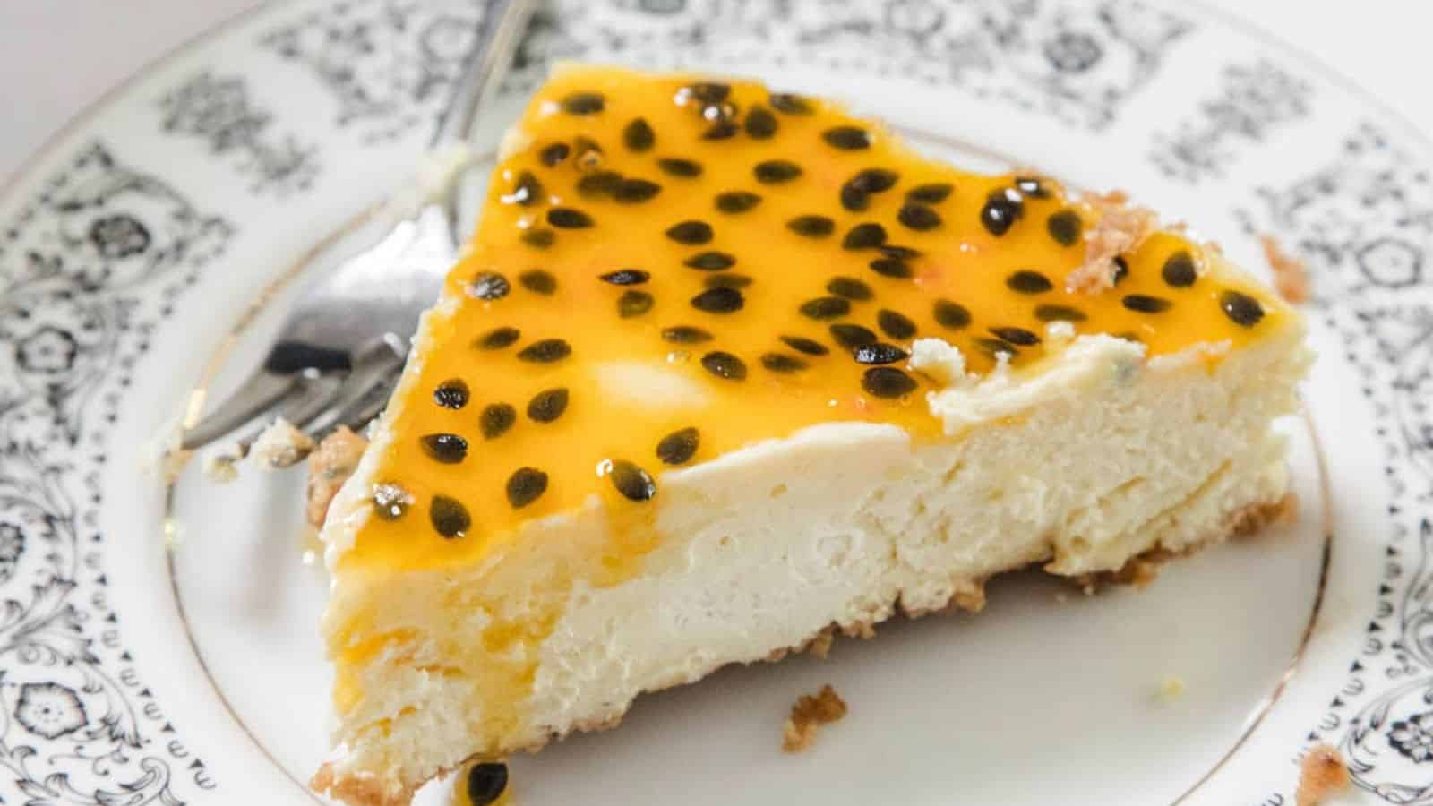 A cheesecake topped with a glossy layer of passion fruit and seeds, with a crumbly biscuit base. A slice has been cut and removed, and two halved passion fruits rest on top of the cheesecake.