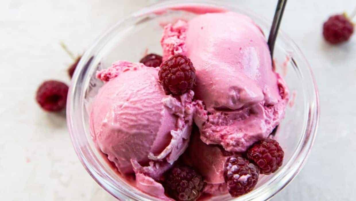 Raspberry Cheesecake Ice Cream with fresh raspberries on top in a glass jar with a spoon.