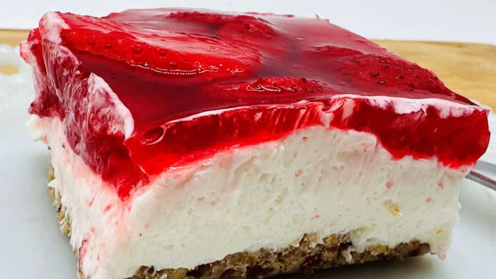 Slice of strawberry pretzel dessert with a layer of strawberries in gelatin, cream cheese filling, and crunchy pretzel crust on a white plate.