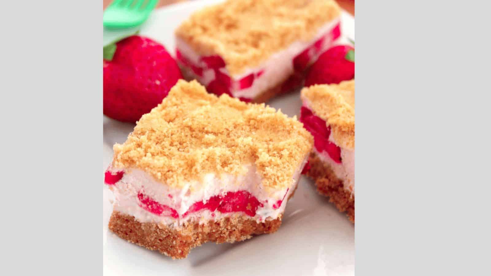 A plate of no bake strawberry bars with a strawberry and green fork in the background.